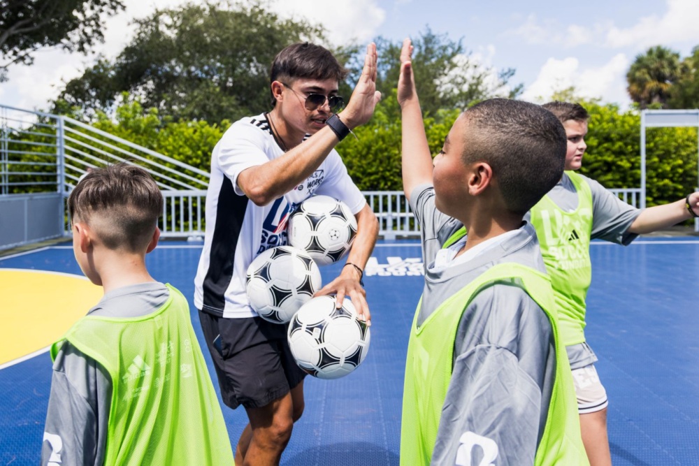 Coach holds 3 soccer balls and high fives a player